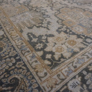 Distressed, low-pile traditional rug featuring an intricate border and floral patterns in gray, tan, and faded blue.