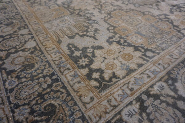 Distressed, low-pile traditional rug featuring an intricate border and floral patterns in gray, tan, and faded blue.