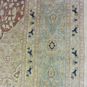 Ornate floral rug with a sage blue field and rust corner accents rests on a dark wood floor.