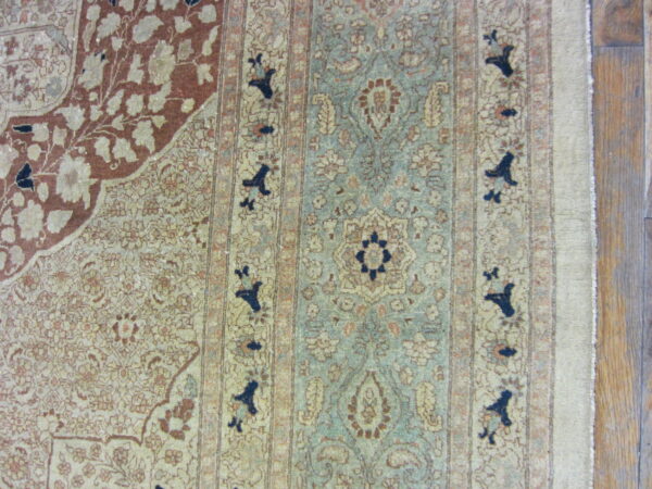 Ornate floral rug with a sage blue field and rust corner accents rests on a dark wood floor.