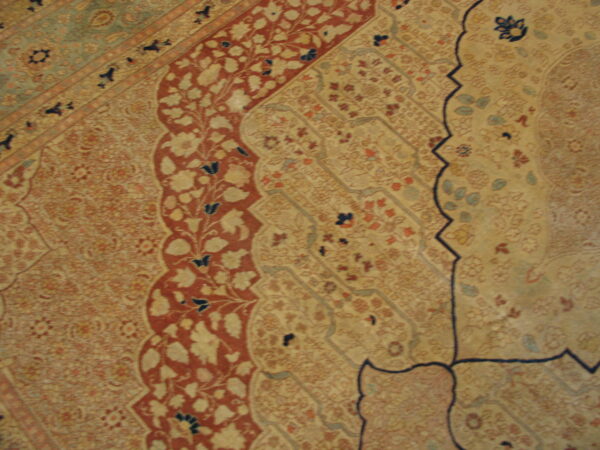 Ornate traditional rug detail showing beige, rust red, and blue floral motifs within curving borders.