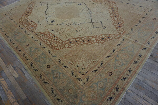 A large traditional rug in beige, rust, and teal floral patterns rests on distressed wood flooring.