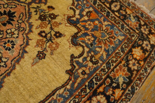Muted gold rug with traditional dark blue and rust floral patterns rests on distressed wooden floors.