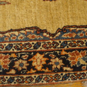 Ornate gold, navy, and rust traditional rug border rests on worn yellow wooden floorboards.