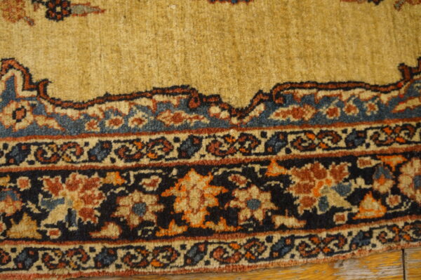 Ornate gold, navy, and rust traditional rug border rests on worn yellow wooden floorboards.