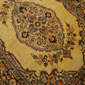 Traditional tan rug with a detailed pink and blue floral medallion and complex dark border on wooden floors.