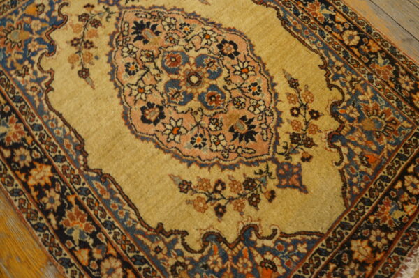 Traditional tan rug with a detailed pink and blue floral medallion and complex dark border on wooden floors.