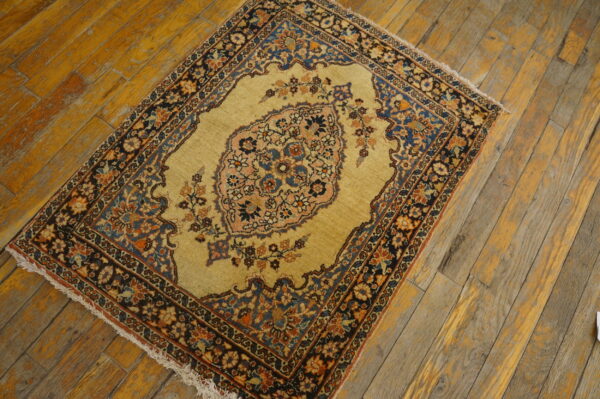 Gold rug with a navy, rust, and pink floral medallion sits on distressed wood flooring.