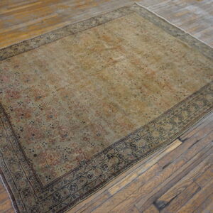 Distressed traditional rug in faded gold and rust colors rests on wide, rustic wooden floorboards.
