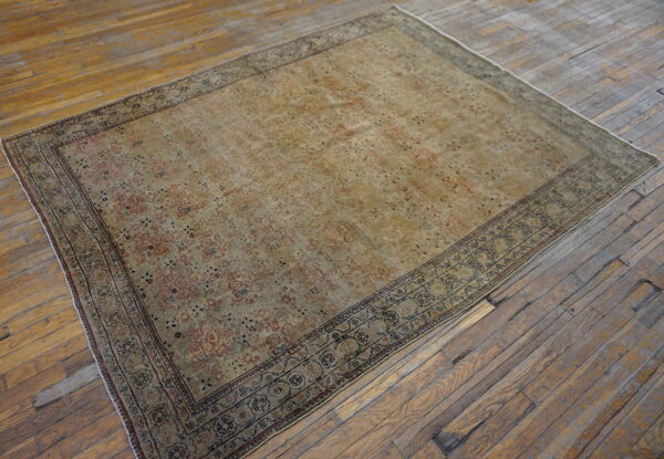 Distressed traditional rug in faded gold and rust colors rests on wide, rustic wooden floorboards.