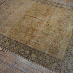 Khaki and rust patterned area rug with a detailed blue border lies on aged, wide plank wood flooring.