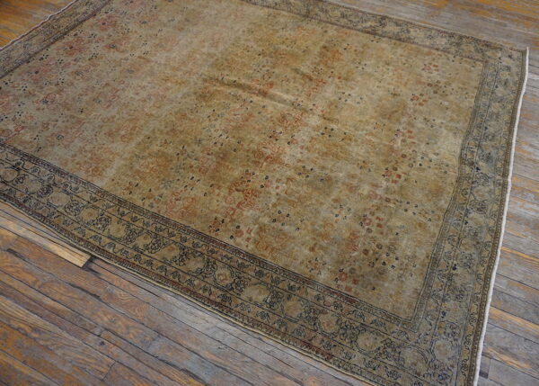 Khaki and rust patterned area rug with a detailed blue border lies on aged, wide plank wood flooring.