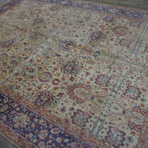 Cream rug featuring intricate floral designs in navy blue and rust, resting on gray wood plank flooring.