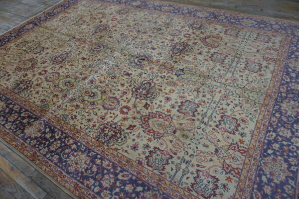 Cream rug featuring intricate floral designs in navy blue and rust, resting on gray wood plank flooring.