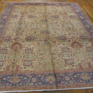 Ornate beige rug with red, blue, and purple floral motifs and a contrasting navy border on wood floor.