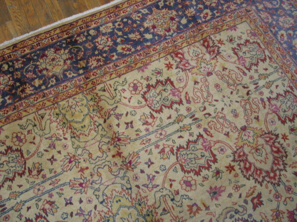 Traditional beige and red floral patterned rug next to a navy blue border on distressed hardwood floors.