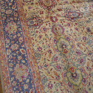 Intricate cream rug with blue and red floral designs and a navy border on hardwood planks.