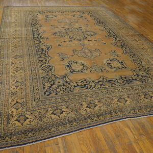 Ornate camel and navy area rug featuring a detailed medallion and multiple borders on wooden flooring.