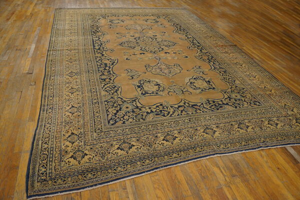 Ornate camel and navy area rug featuring a detailed medallion and multiple borders on wooden flooring.