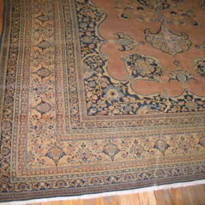 Rosy pink traditional rug with complex navy and beige borders displayed on light hardwood floors.