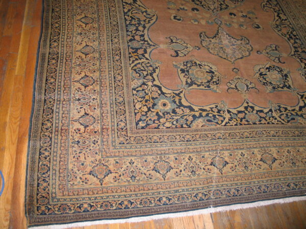 Rosy pink traditional rug with complex navy and beige borders displayed on light hardwood floors.