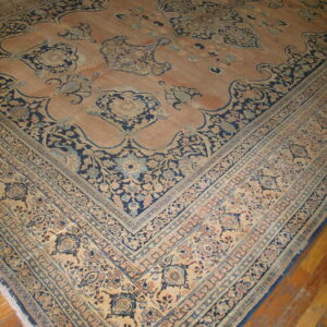 Large traditional rug with a peach field and intricate navy blue and beige floral borders on wood floorboards.