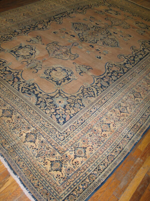Large traditional rug with a peach field and intricate navy blue and beige floral borders on wood floorboards.