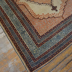 A cream rug with elaborate orange, blue, and navy borders rests on rustic wood plank flooring.