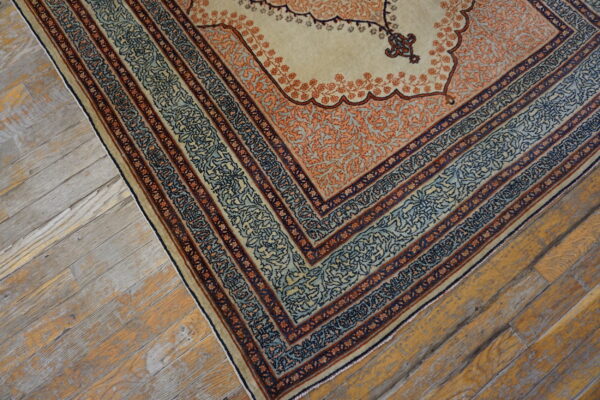 A cream rug with elaborate orange, blue, and navy borders rests on rustic wood plank flooring.