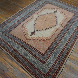 Low pile rug in cream, peach, and slate blue with an ornate medallion on rustic wood flooring.
