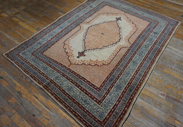Low pile rug in cream, peach, and slate blue with an ornate medallion on rustic wood flooring.