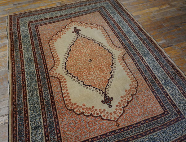 Traditional low-pile rug with a cream field, rust medallion, and navy-blue borders rests on distressed wood flooring.
