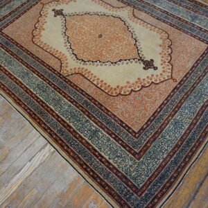 Cream rug with a detailed orange medallion and layered blue borders sits on distressed hardwood flooring.