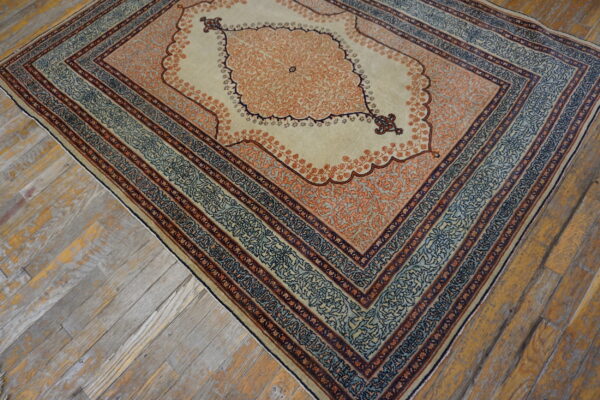 Cream rug with a detailed orange medallion and layered blue borders sits on distressed hardwood flooring.