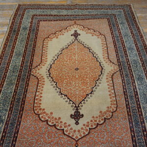Burnt orange and beige medallion rug with blue accents lies on distressed wooden floorboards.
