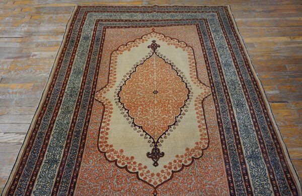 Burnt orange and beige medallion rug with blue accents lies on distressed wooden floorboards.