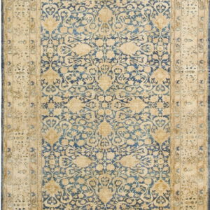 A traditional rug featuring a blue field with cream and gold floral motifs and wide tan borders.