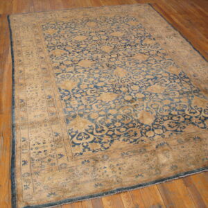 Low-pile blue and tan traditional rug with ornate pattern covering wide plank wood flooring.