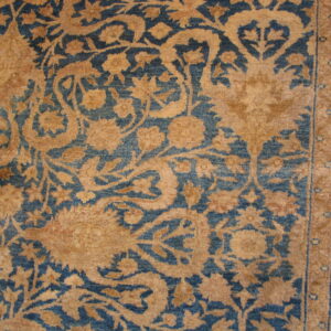 Tan and blue rug close-up showing intricate botanical patterns and a multi-band vertical border.