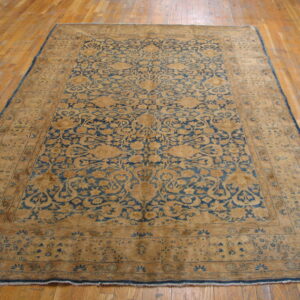 Tan and faded blue ornate traditional rug placed on a shiny light wood plank floor.