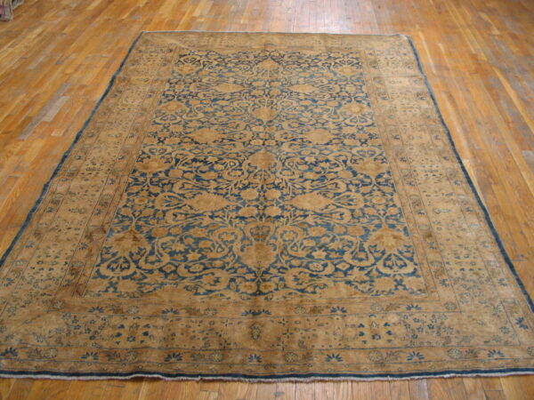 Tan and faded blue ornate traditional rug placed on a shiny light wood plank floor.