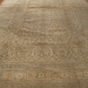 Large, faded beige and brown traditional rug featuring ogee lattice and a wide border over hardwood flooring.