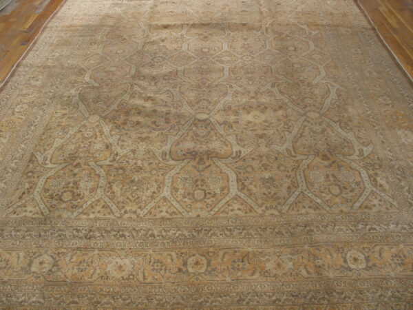 Large, faded beige and brown traditional rug featuring ogee lattice and a wide border over hardwood flooring.