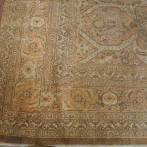 Faded tan and ochre traditional rug featuring complex floral borders on a distressed wood floor.