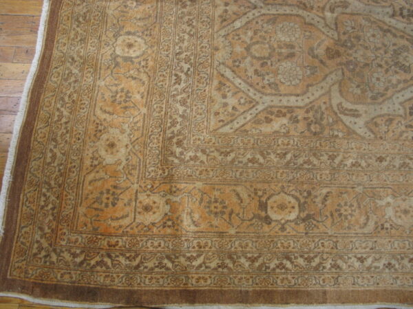 Faded tan and ochre traditional rug featuring complex floral borders on a distressed wood floor.