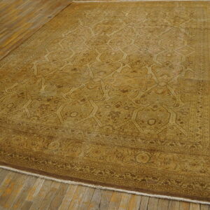 Large, traditional gold and brown rug with an intricate pattern lying on distressed hardwood planks.