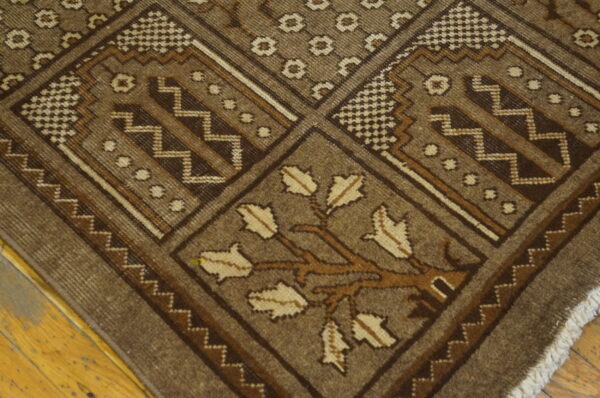 Detail of a brown geometric rug featuring checkered and zigzag borders and a stylized tree motif on hardwood.