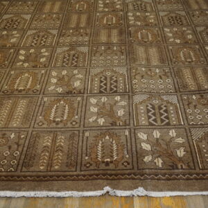 Low pile brown rug with a repeating checkerboard of stylized geometric and botanical squares on a wood floor.