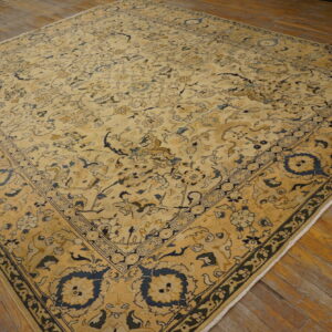 Intricate gold and ivory traditional rug with dark blue motifs shown on rustic plank wood flooring.