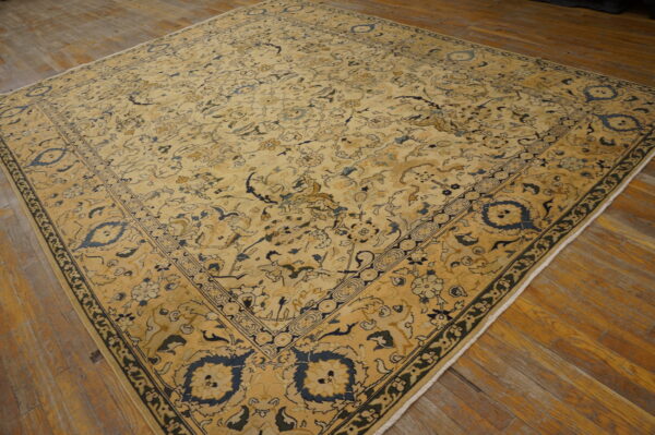 Intricate gold and ivory traditional rug with dark blue motifs shown on rustic plank wood flooring.